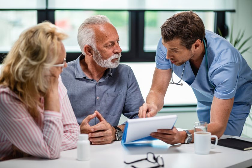 Serious doctor discussing with senior couple about their medical documents appointment clinic